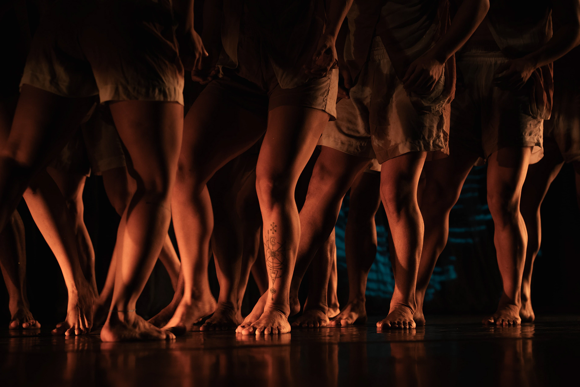 Bailarinos em cena com iluminação em tons laranja e vermelho